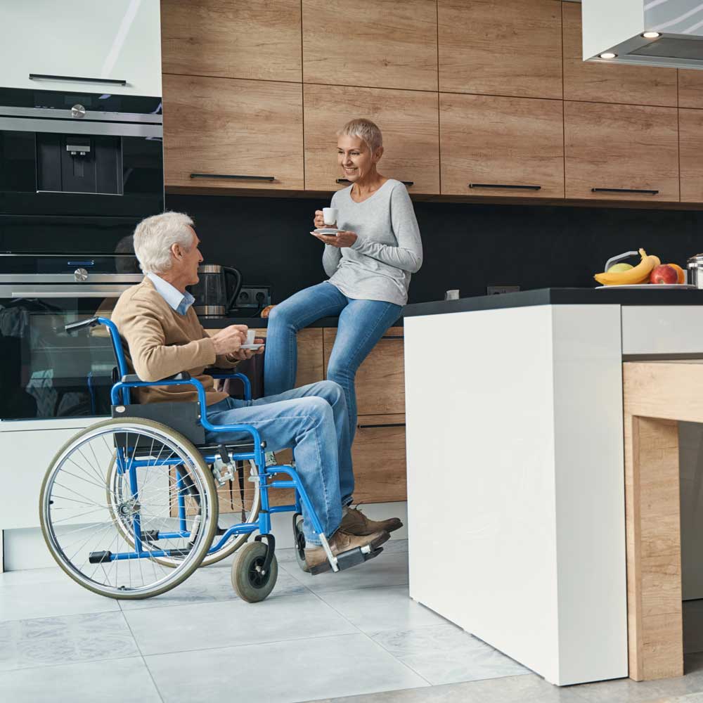 A man in a wheelchair visits with a woman in a kitchen