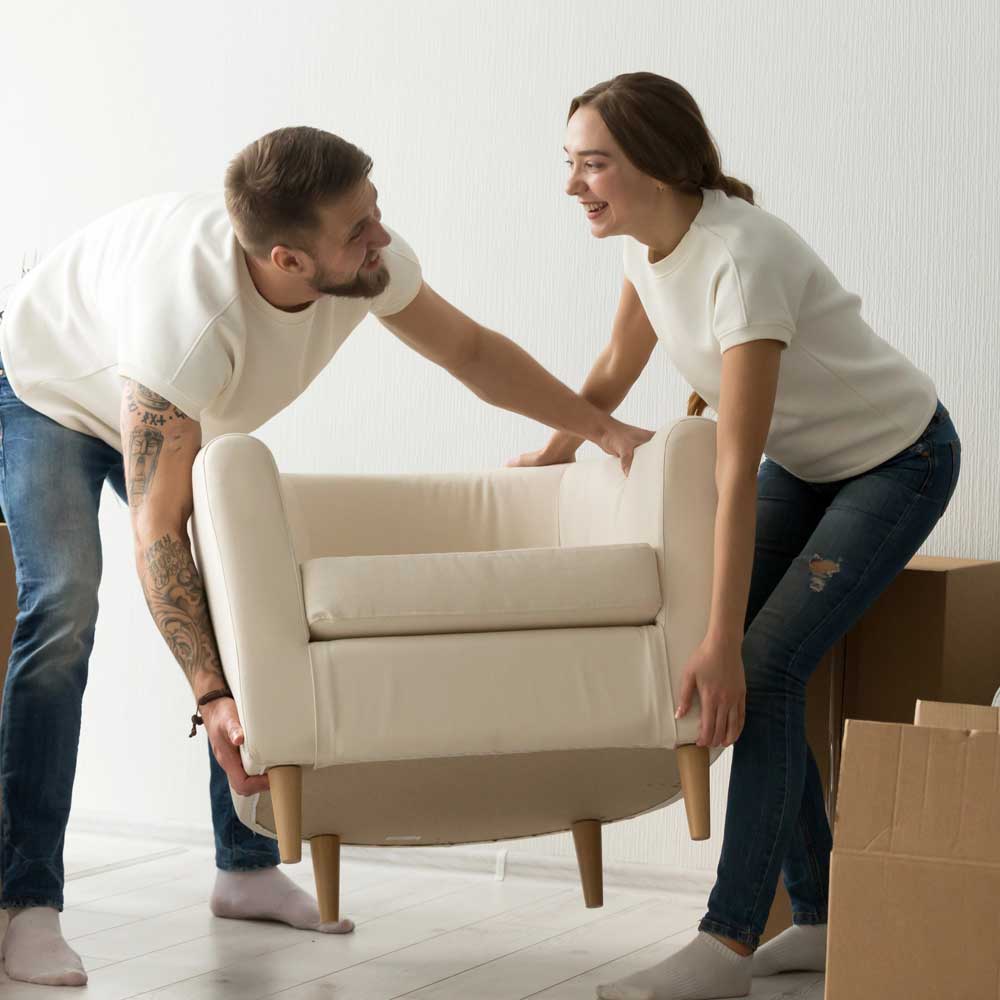 Young couple carrying chair together, placing furniture
