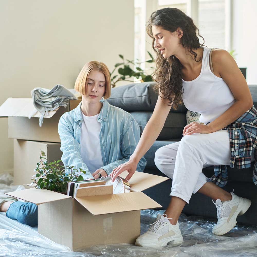 Young brunette woman taking clock out of cardboard box